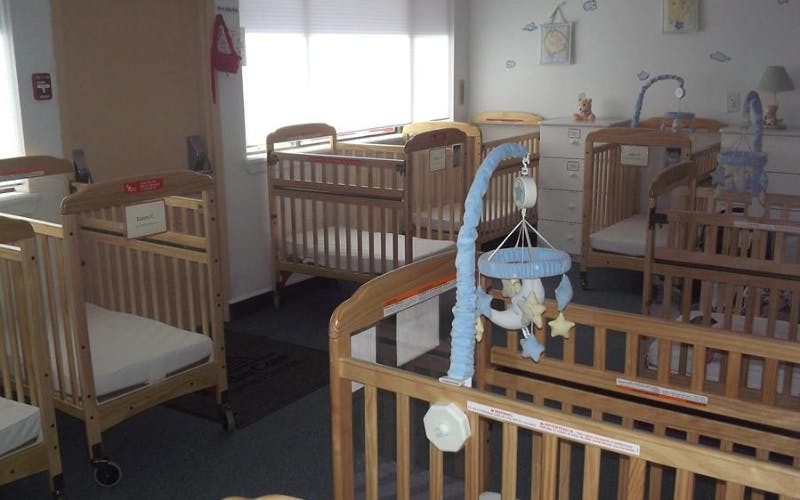 Multiple wooden cribs in a room, some with attached mobiles