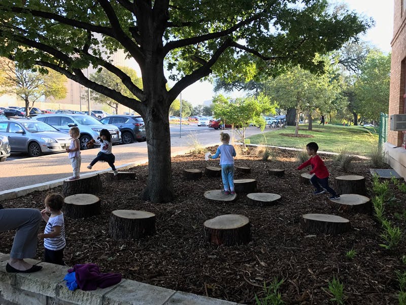 Children playing on tree stumps under a large tree