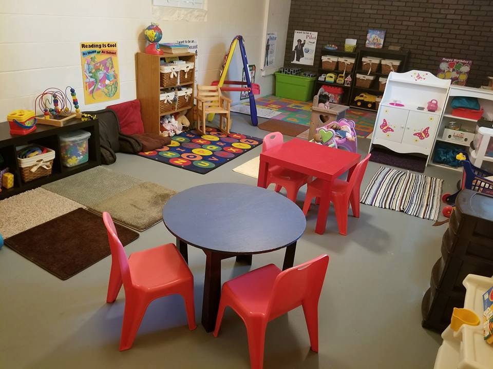 Playroom with small tables and chairs, colorful rugs, and shelves with toys