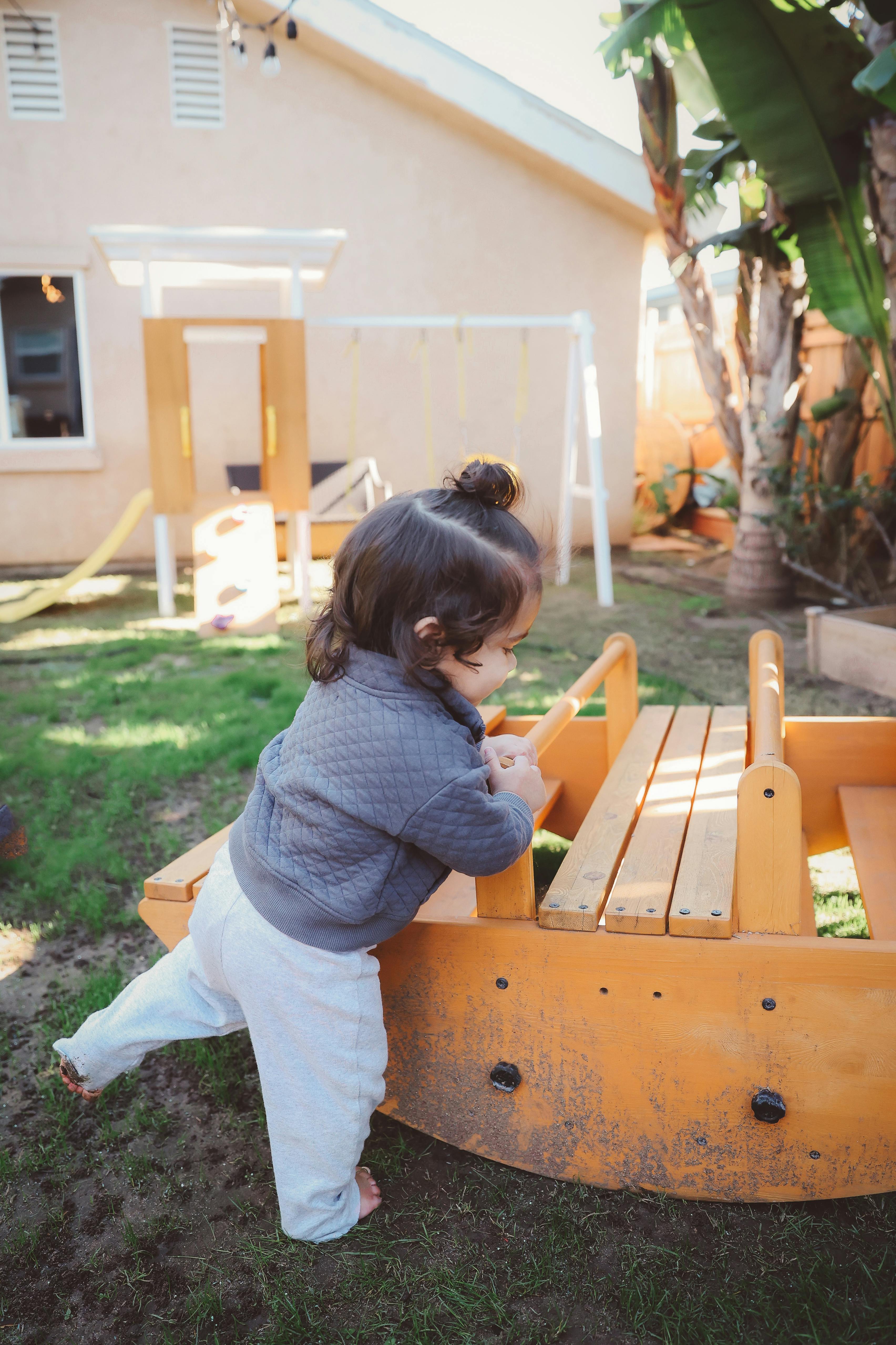 Child standing barefoot in grass, leaning on a wooden toy