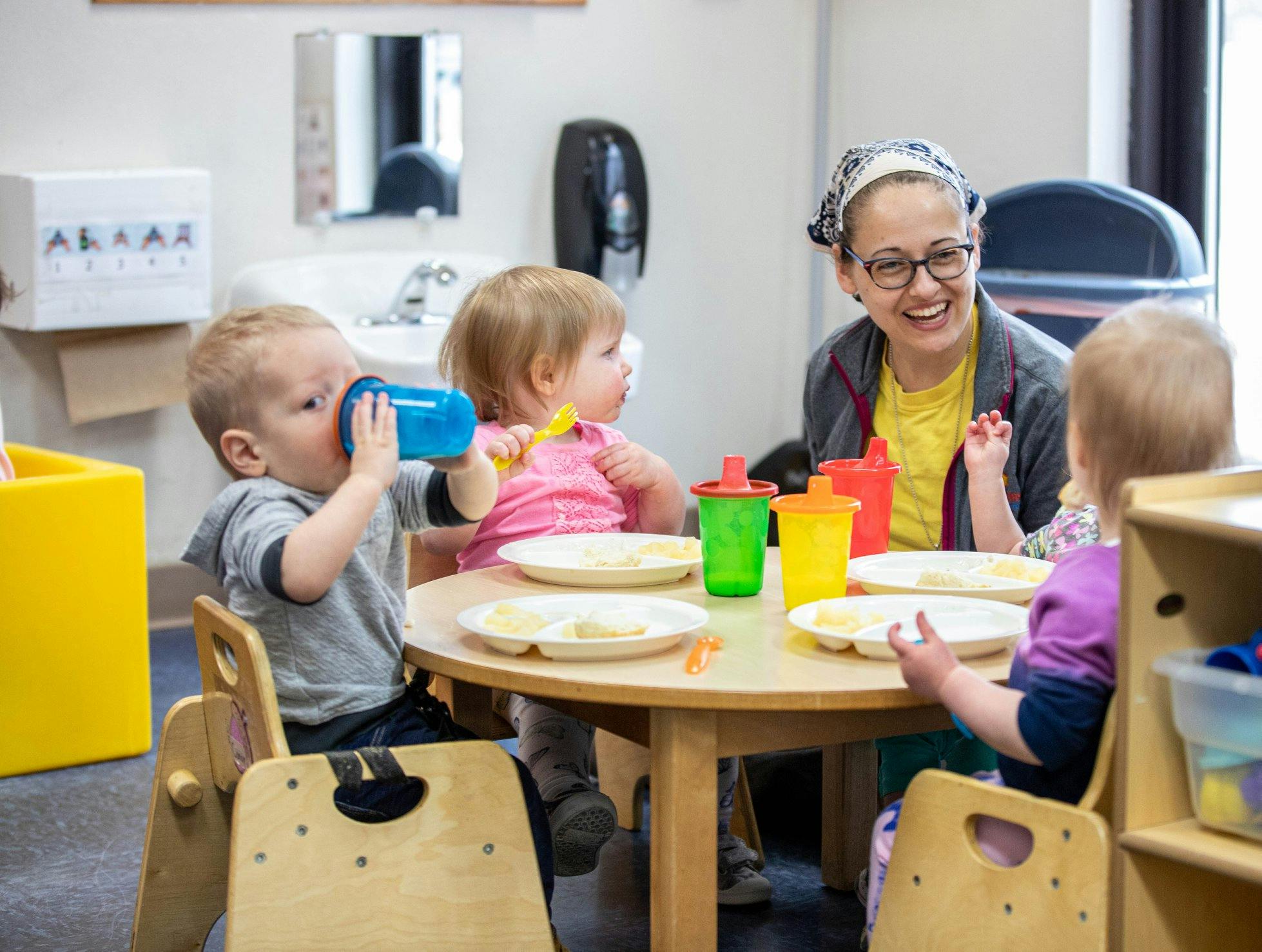 Adult and three children sitting at a table with plates and cups