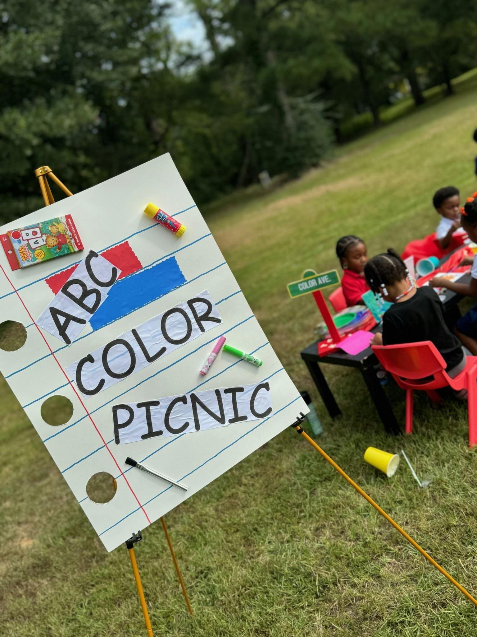 Easel with a sign that reads "ABC Color Picnic" with children sitting at a table