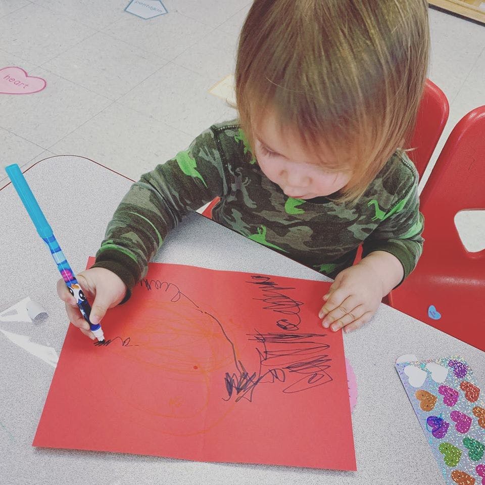 Child drawing on red paper with a blue marker