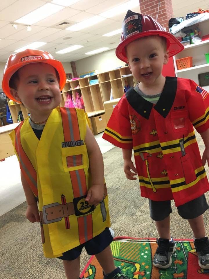 Two children in dress-up costumes, one in a construction worker outfit and one in a firefighter outfit