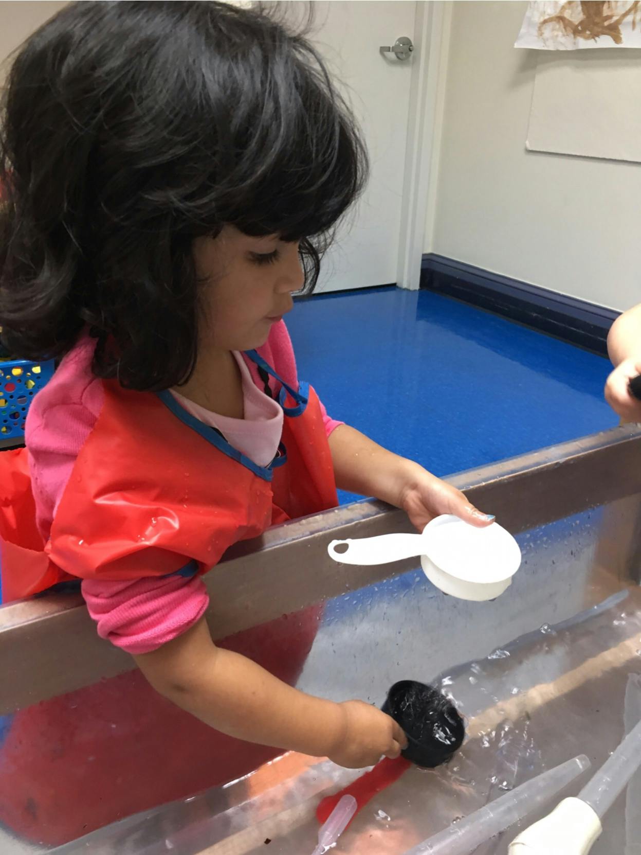 Child playing with water and scoops in a sensory bin