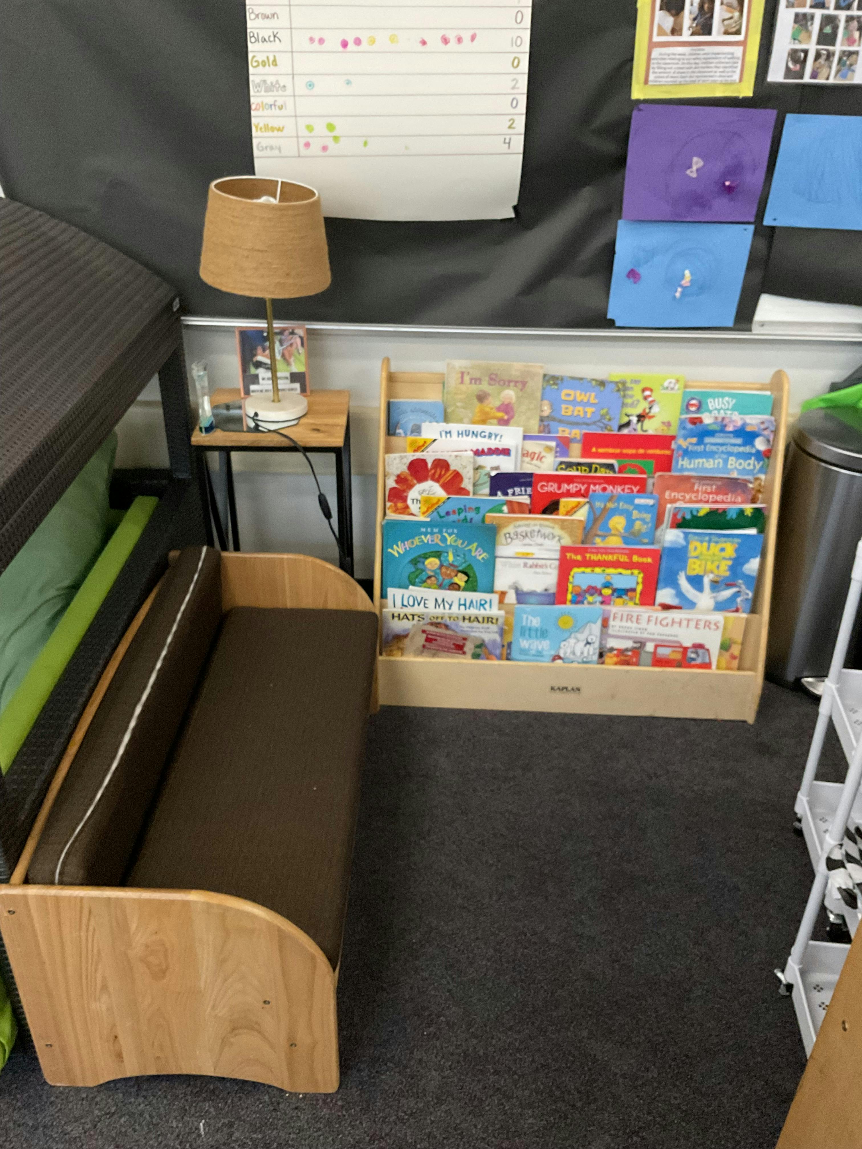 A wooden bench with a brown cushion next to a bookshelf filled with children's books