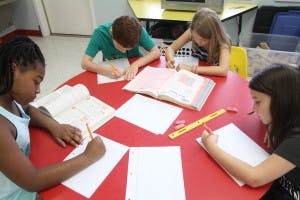 Four children writing at a red table in a classroom