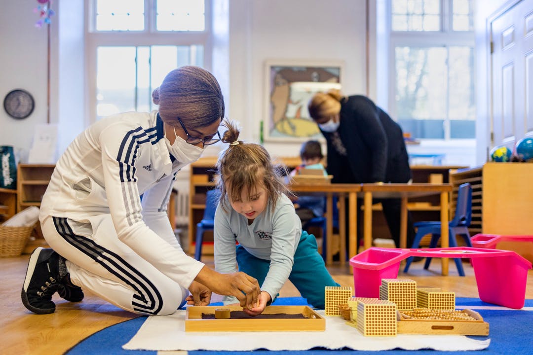 Adult and child on floor engaging with learning materials in a classroom