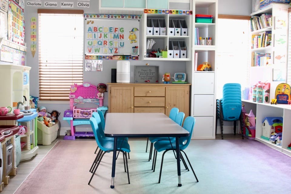 Classroom with a table and blue chairs, shelves, and a whiteboard with ABCs