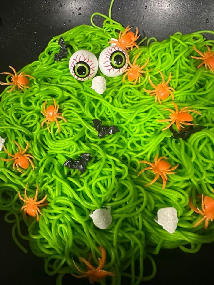 Green spaghetti with plastic spiders, bats, eyeballs, and skulls