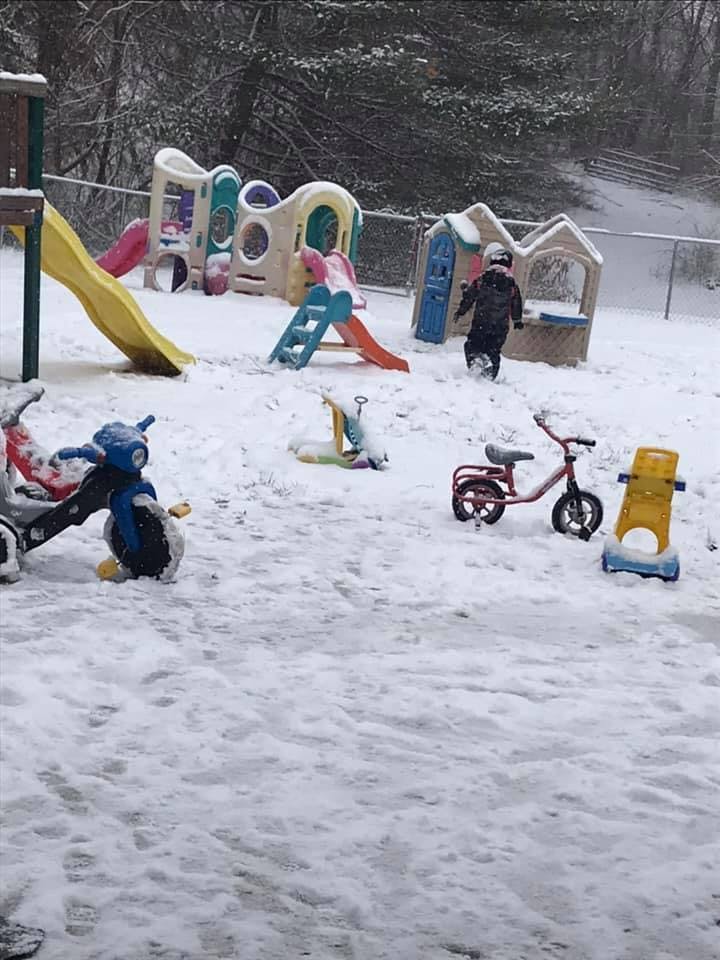 Child walking in snow on a playground with play structures and toys