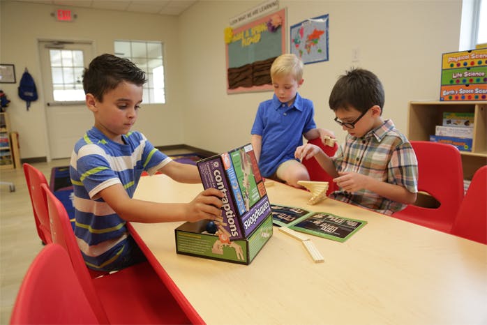 Three children playing with games at a table in a classroom