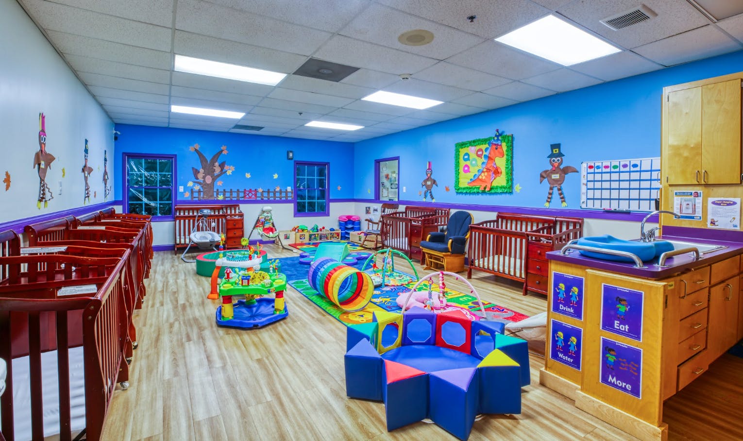 A colorful daycare room with cribs, play mats, and a changing station