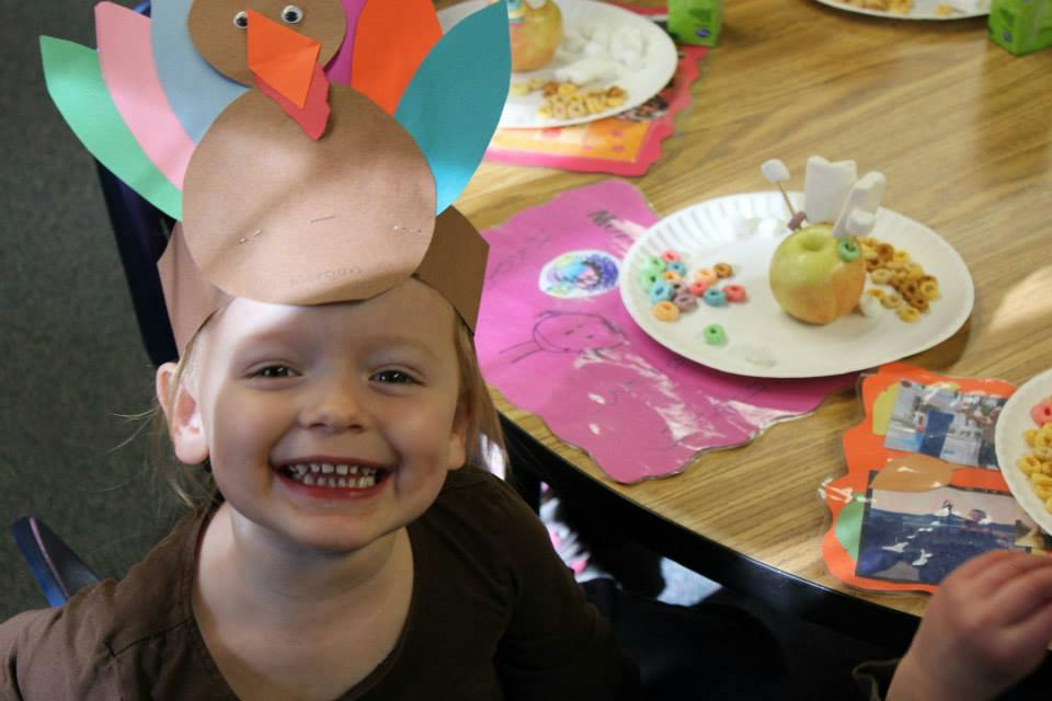 Child wearing a turkey hat at a table with plates of food