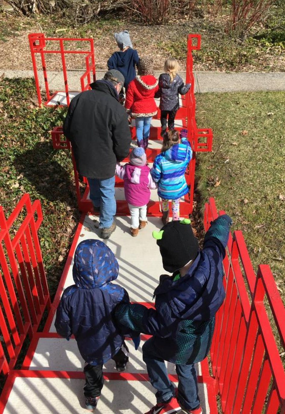 Adult and children walking up red outdoor stairs