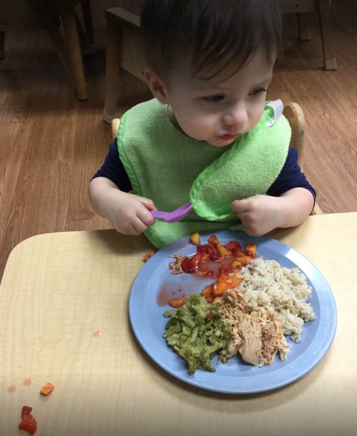 Child in a bib eating from a plate with a fork