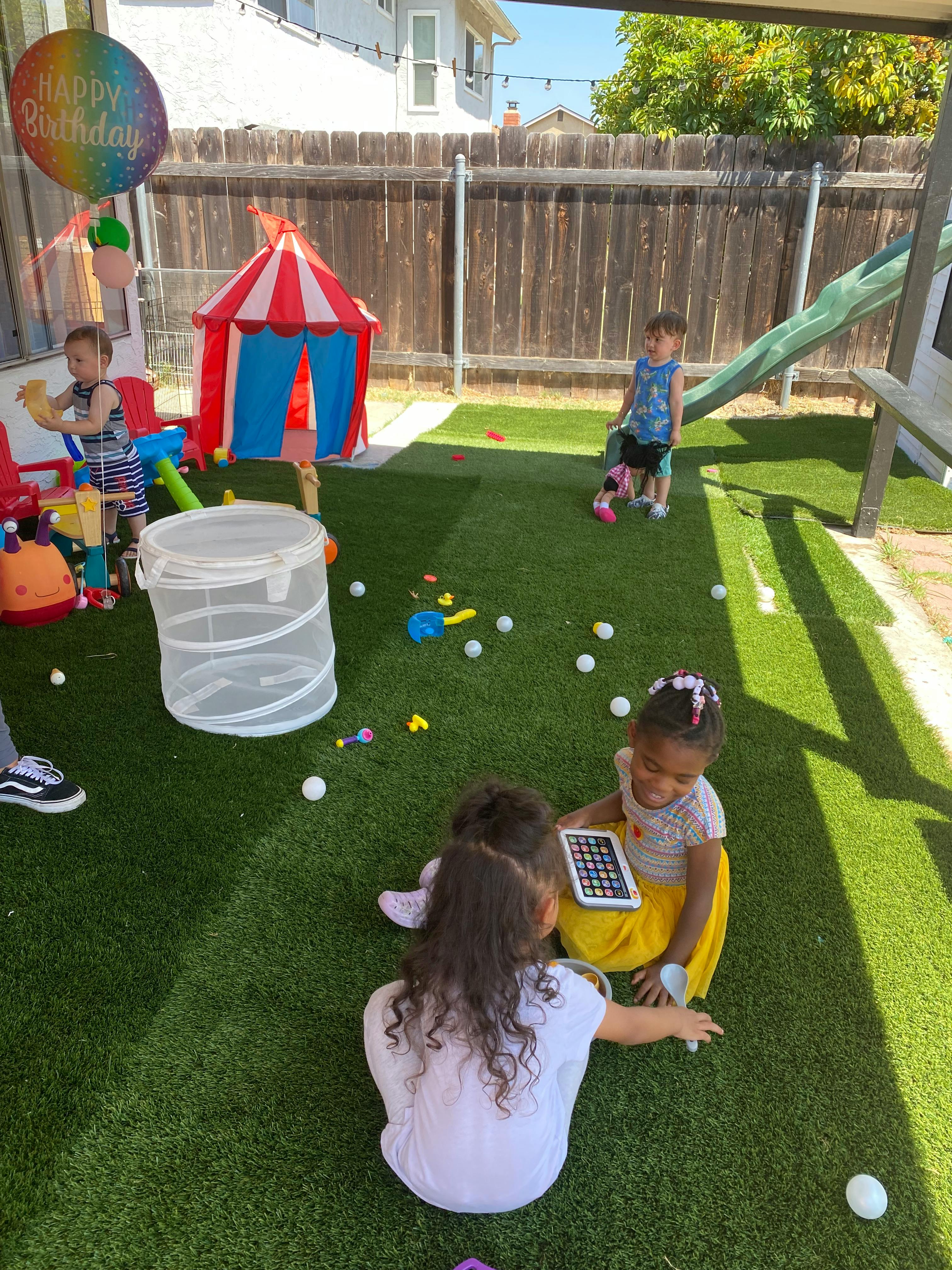 Children playing outdoors with toys and a tablet