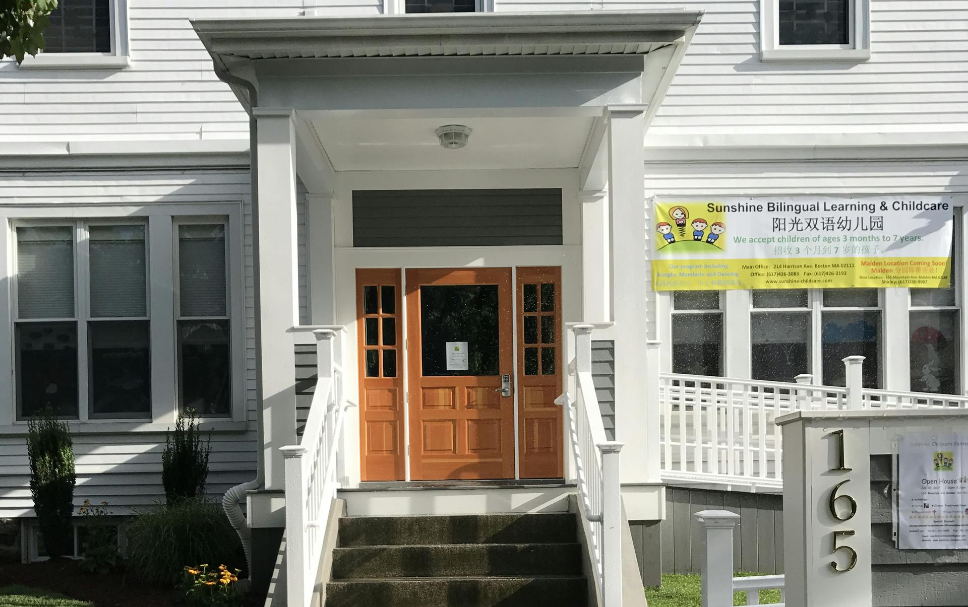 Front entrance of a white building with brown doors and a sign