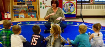 Adult person sitting on floor with children in front of children in a group of children