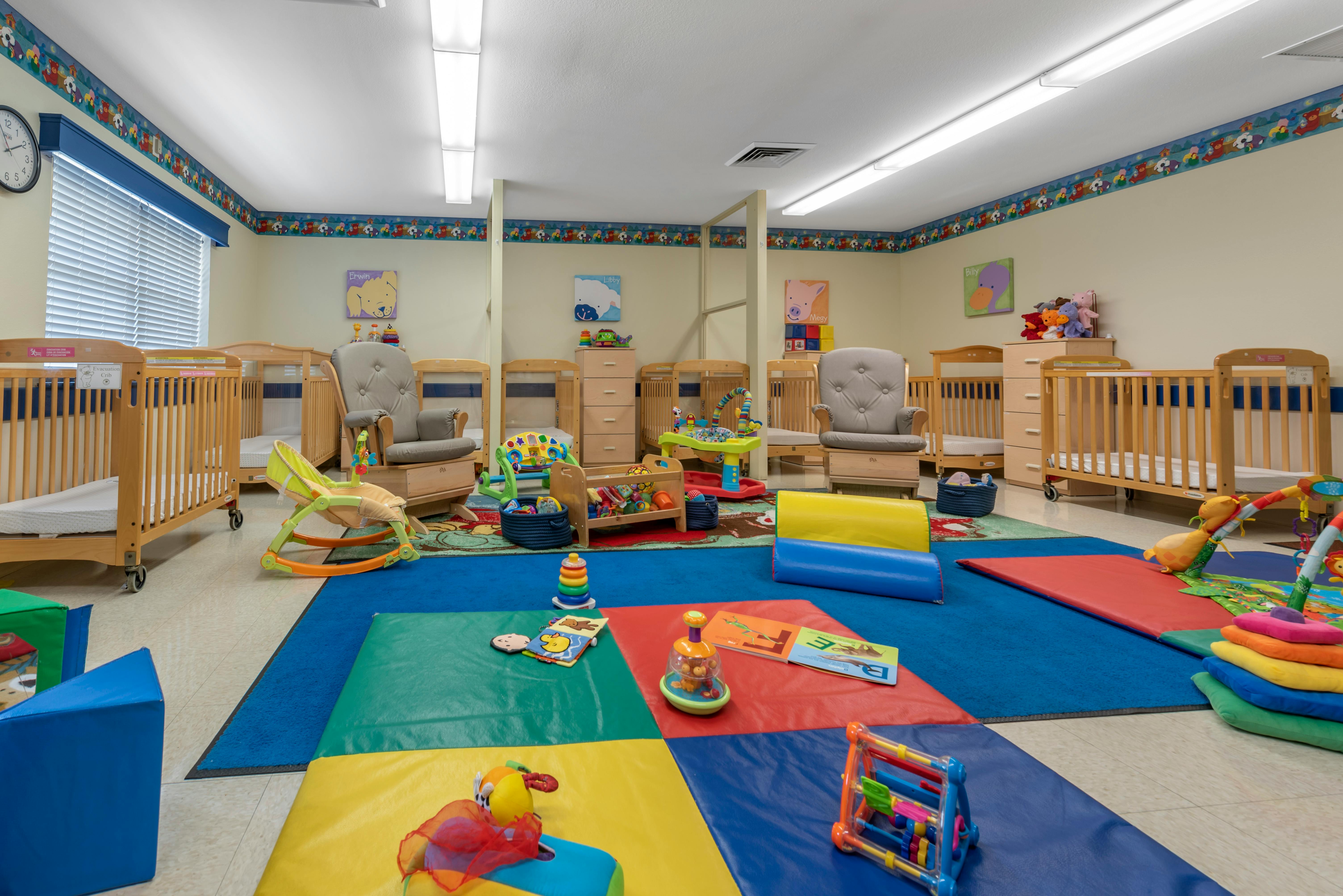 Baby room with multiple cribs, a rocking chair, and play mats with toys