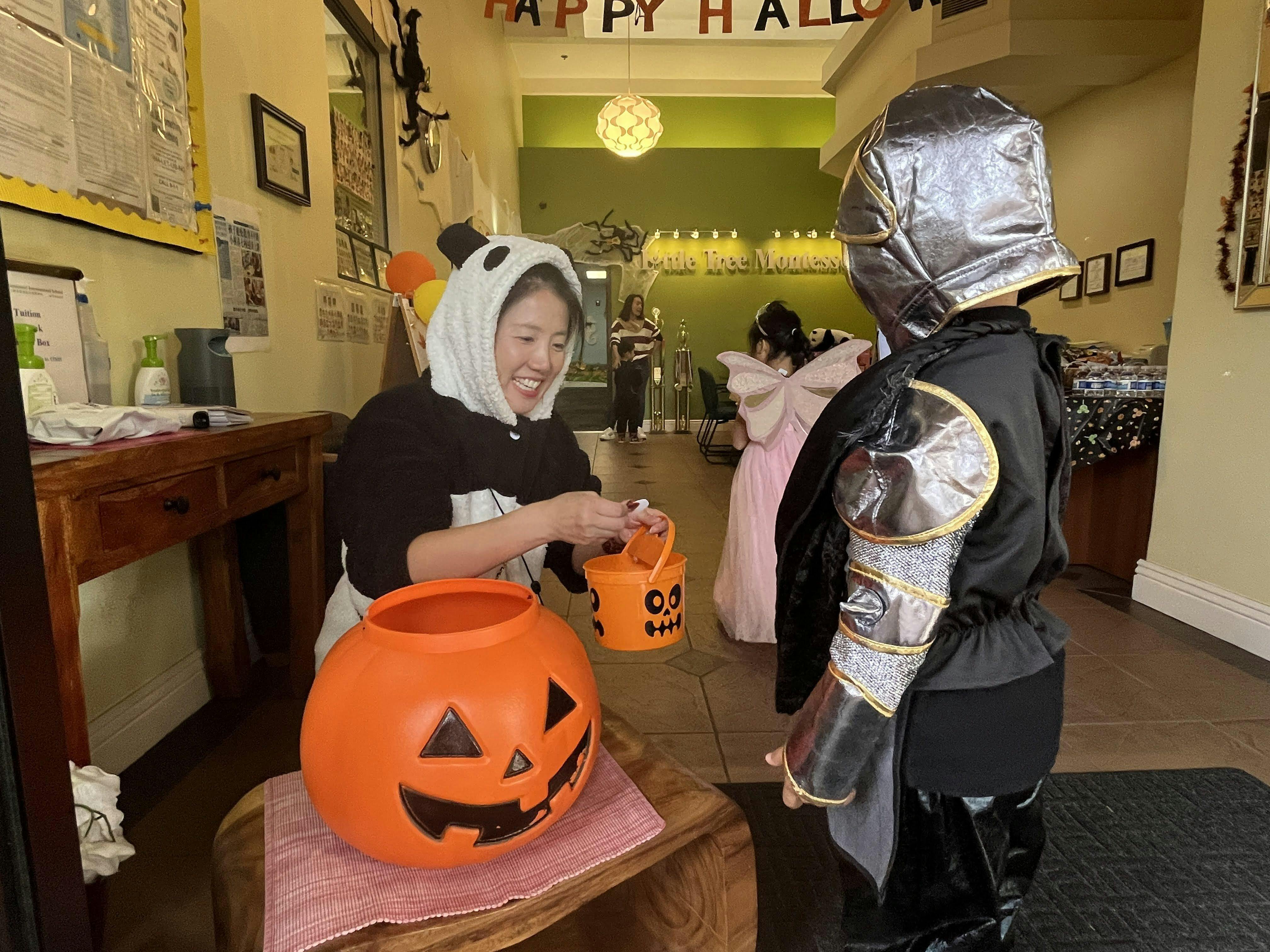 Person in a panda costume giving candy to a child in a knight costume