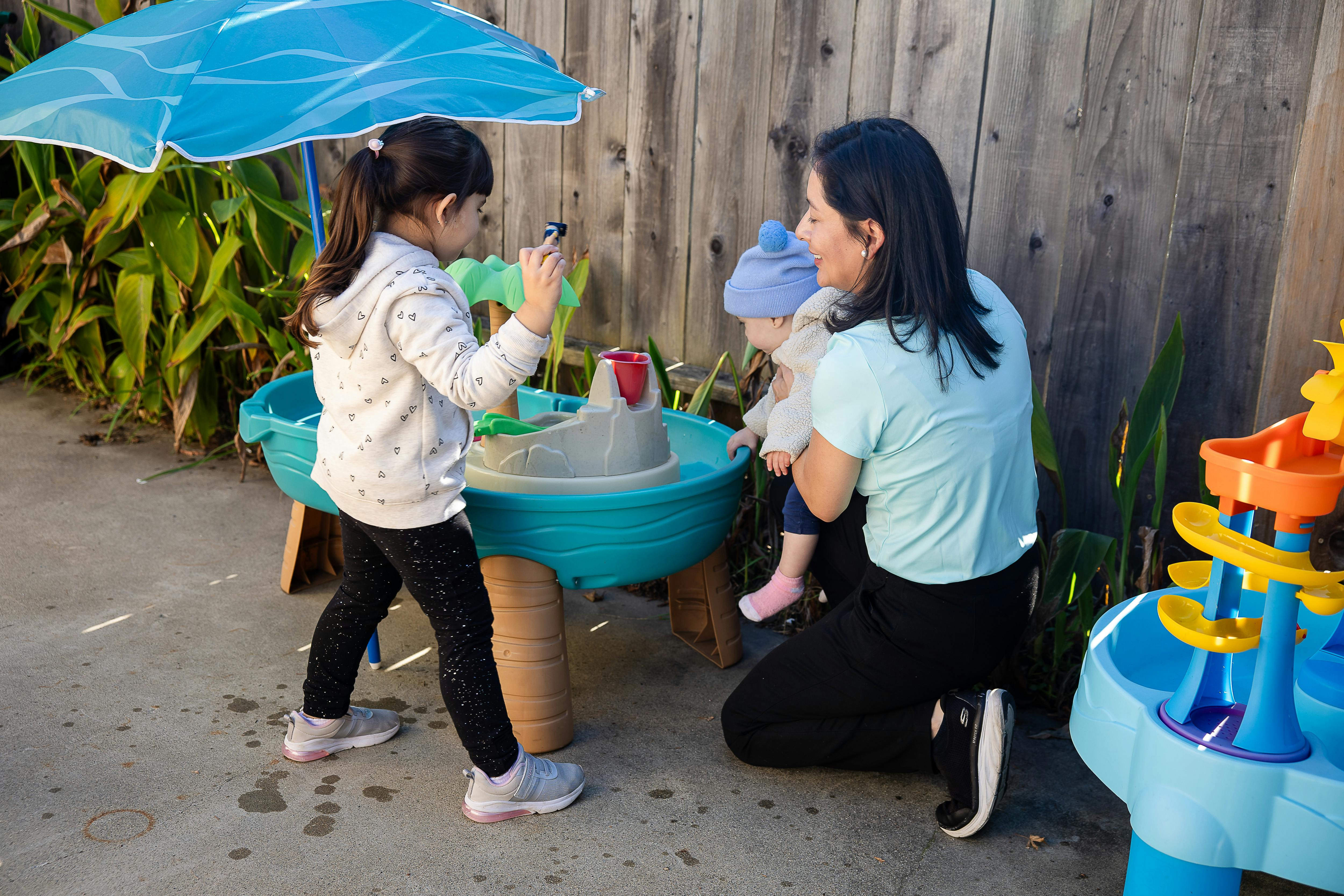 Person holding a child while another child plays at a water table