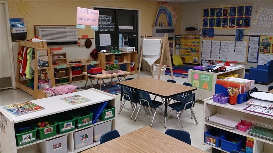 empty preschool classroom with tables, chairs, and shelves of toys and learning materials