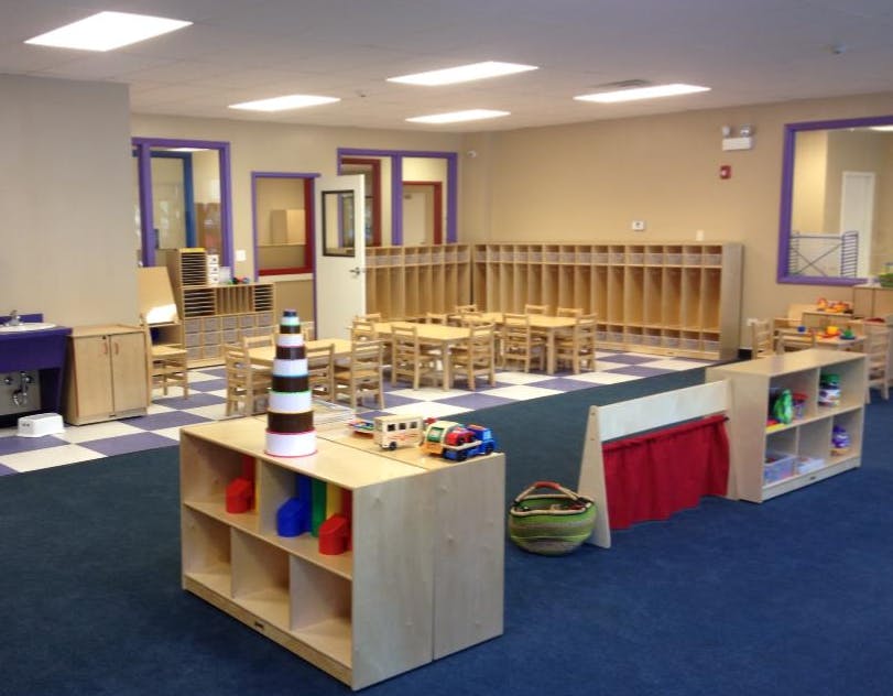 Empty classroom with small tables and chairs, shelves with toys