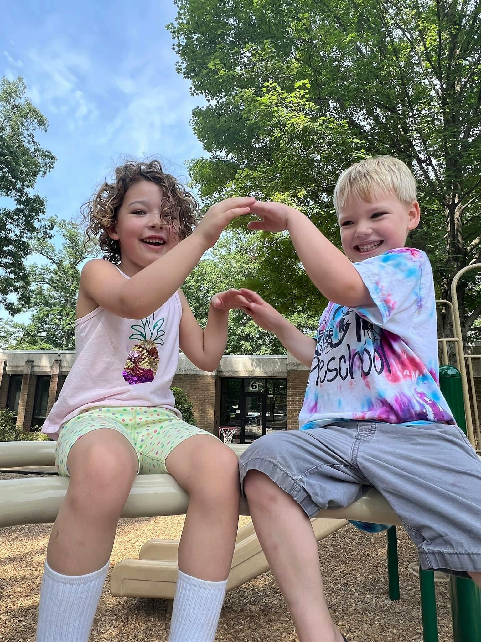 Two children sitting on playground equipment playing hand games