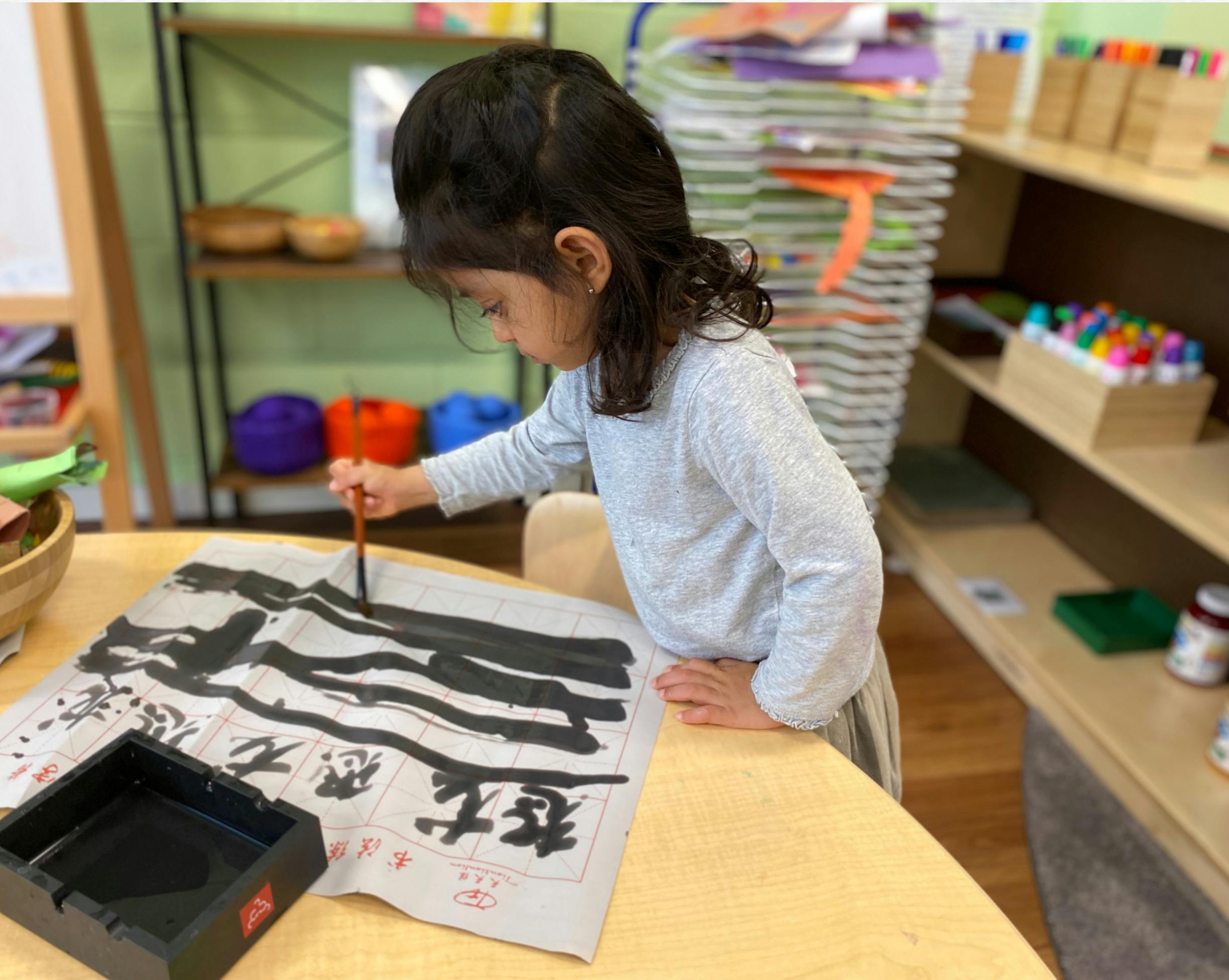 Child practicing Chinese calligraphy with a brush on a paper grid
