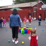Adult and children playing with colorful blocks and balls outdoors