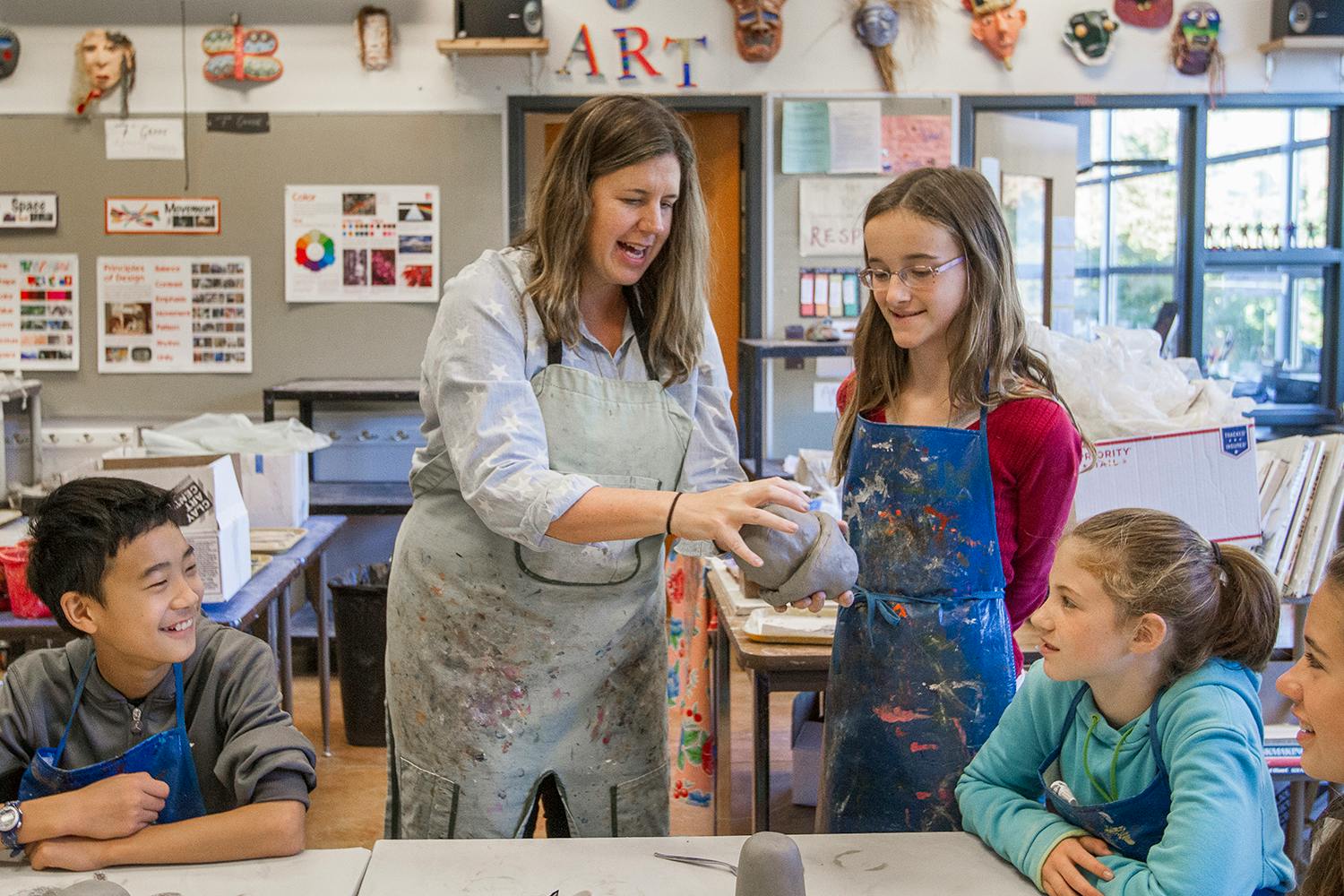Adult showing three children how to work with clay in an art classroom