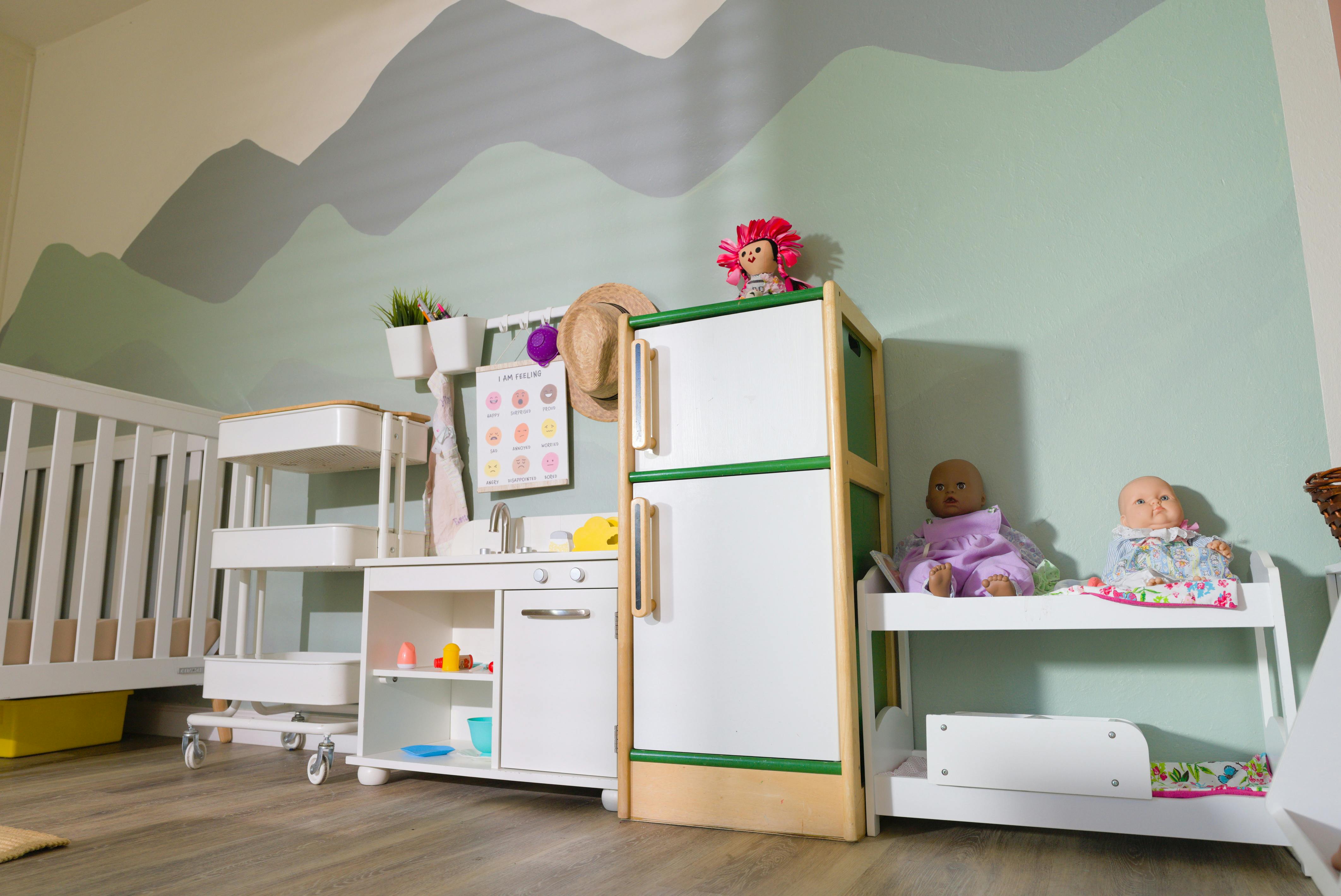 Child's play kitchen and refrigerator with dolls, a crib, and a feelings chart