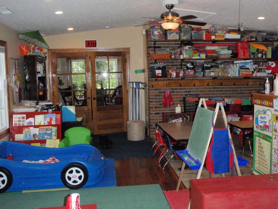 Playroom with a blue toy car, tables, chairs, and shelves filled with items