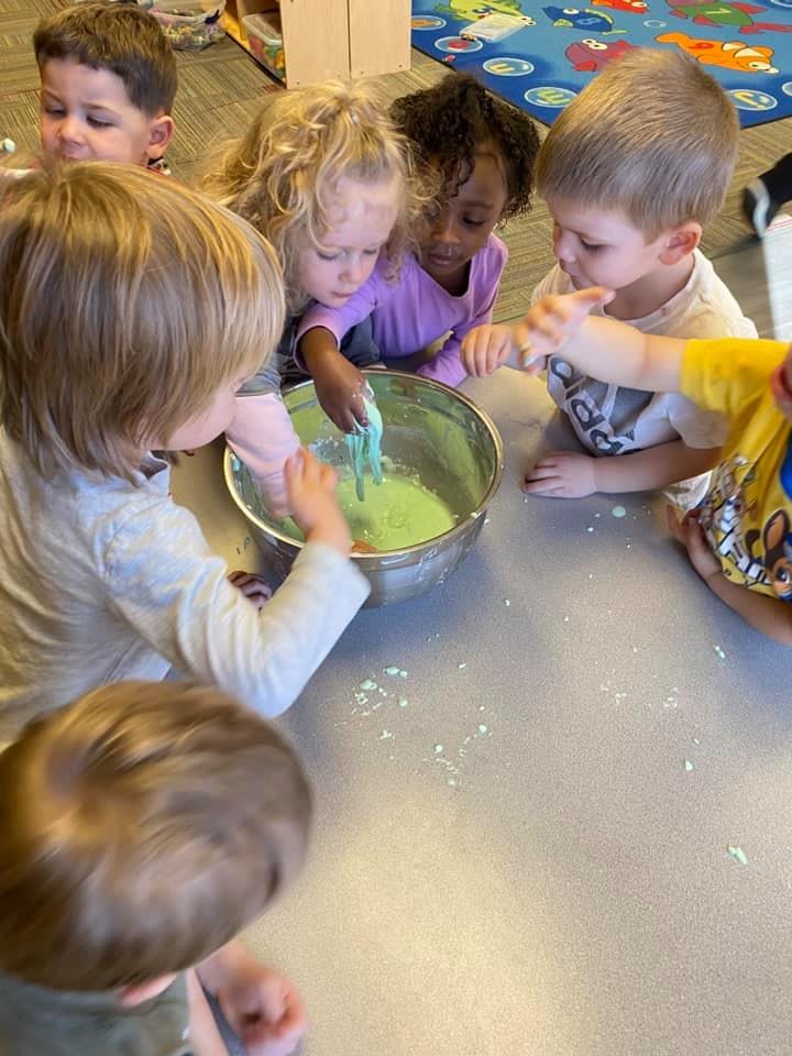 Children gathered around a bowl, playing with green slime
