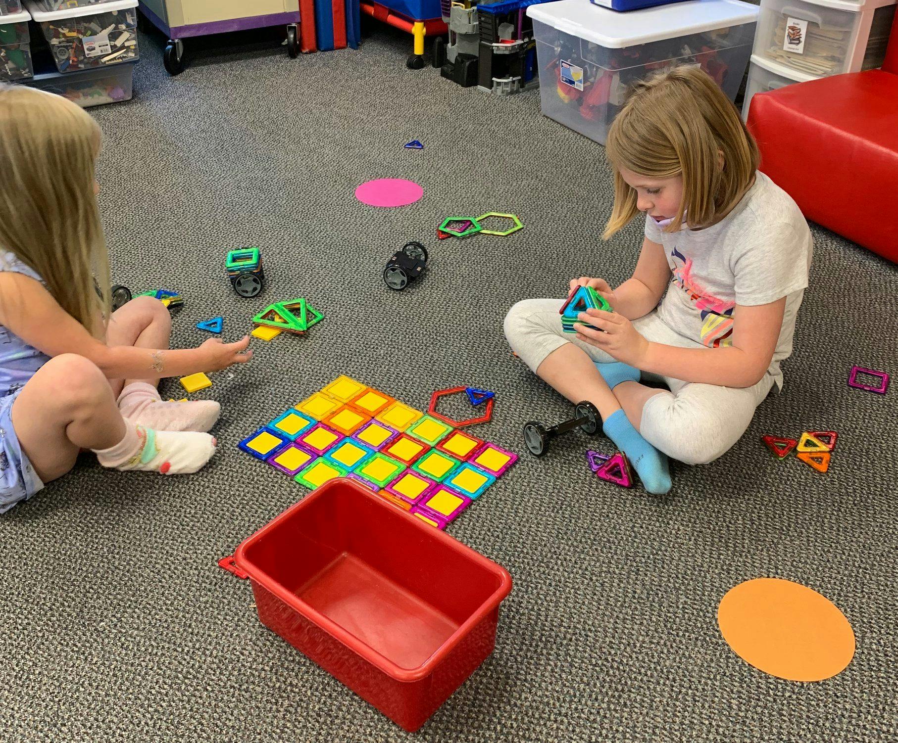 Two children playing with colorful building toys on a carpeted floor