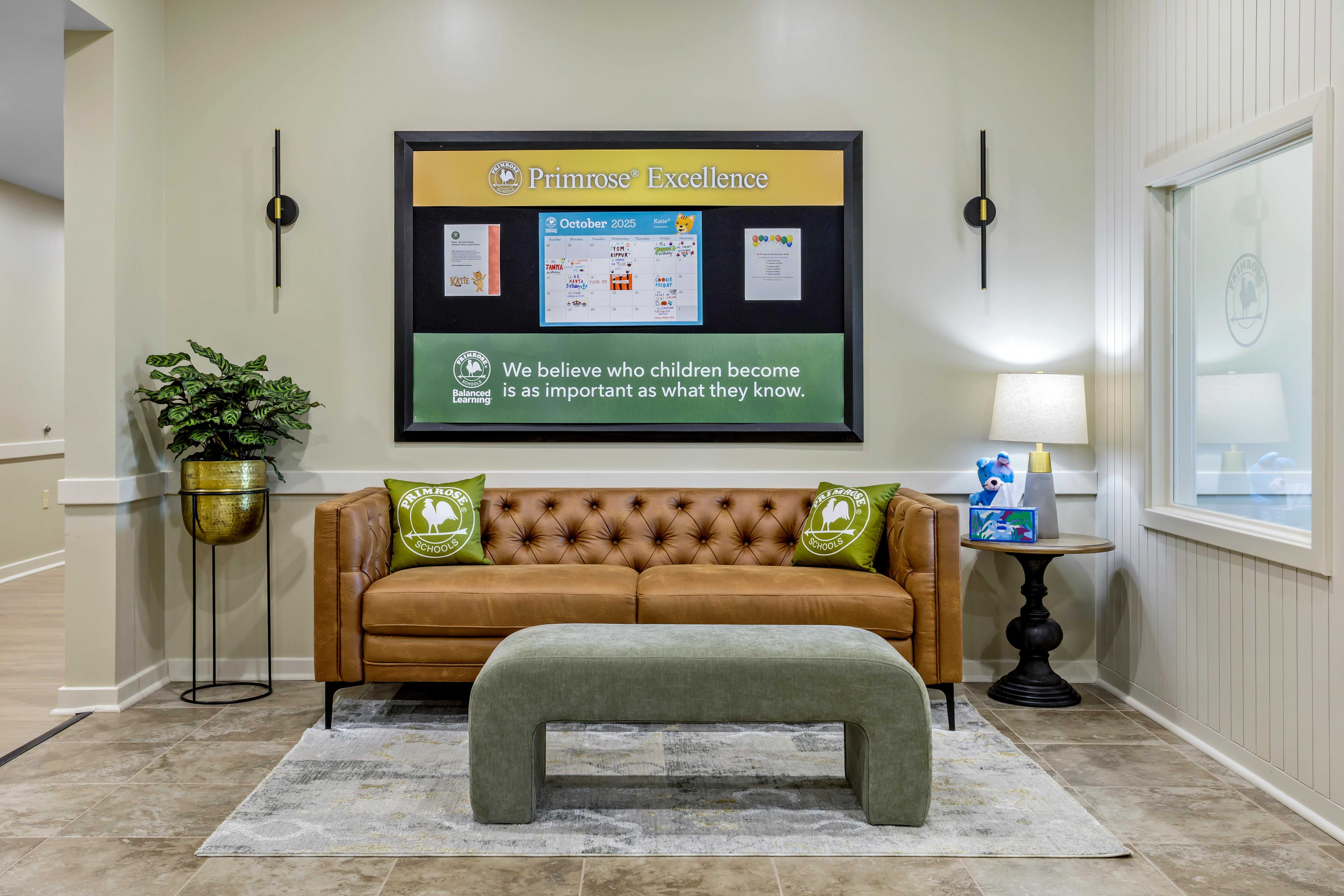 Lounge area with a brown leather couch, green ottoman, and Primrose Schools signage