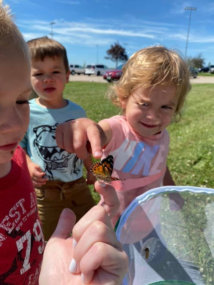 Child pointing at a butterfly on a person's finger