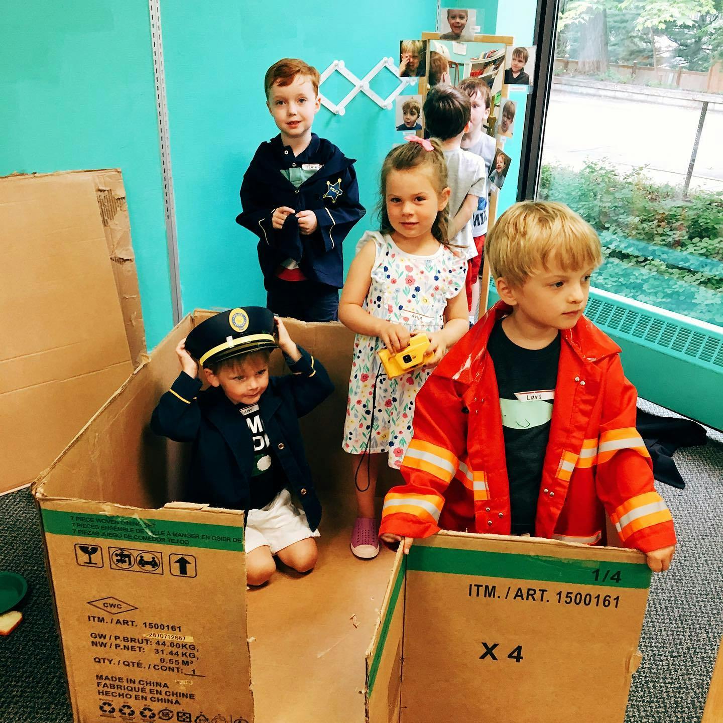 Children playing in cardboard boxes, one in a pilot hat, one in a firefighter jacket
