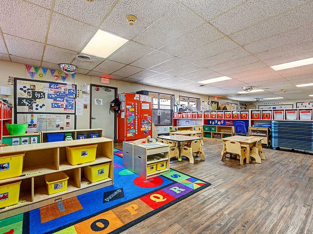 An empty childcare classroom with small tables, chairs, and colorful rug