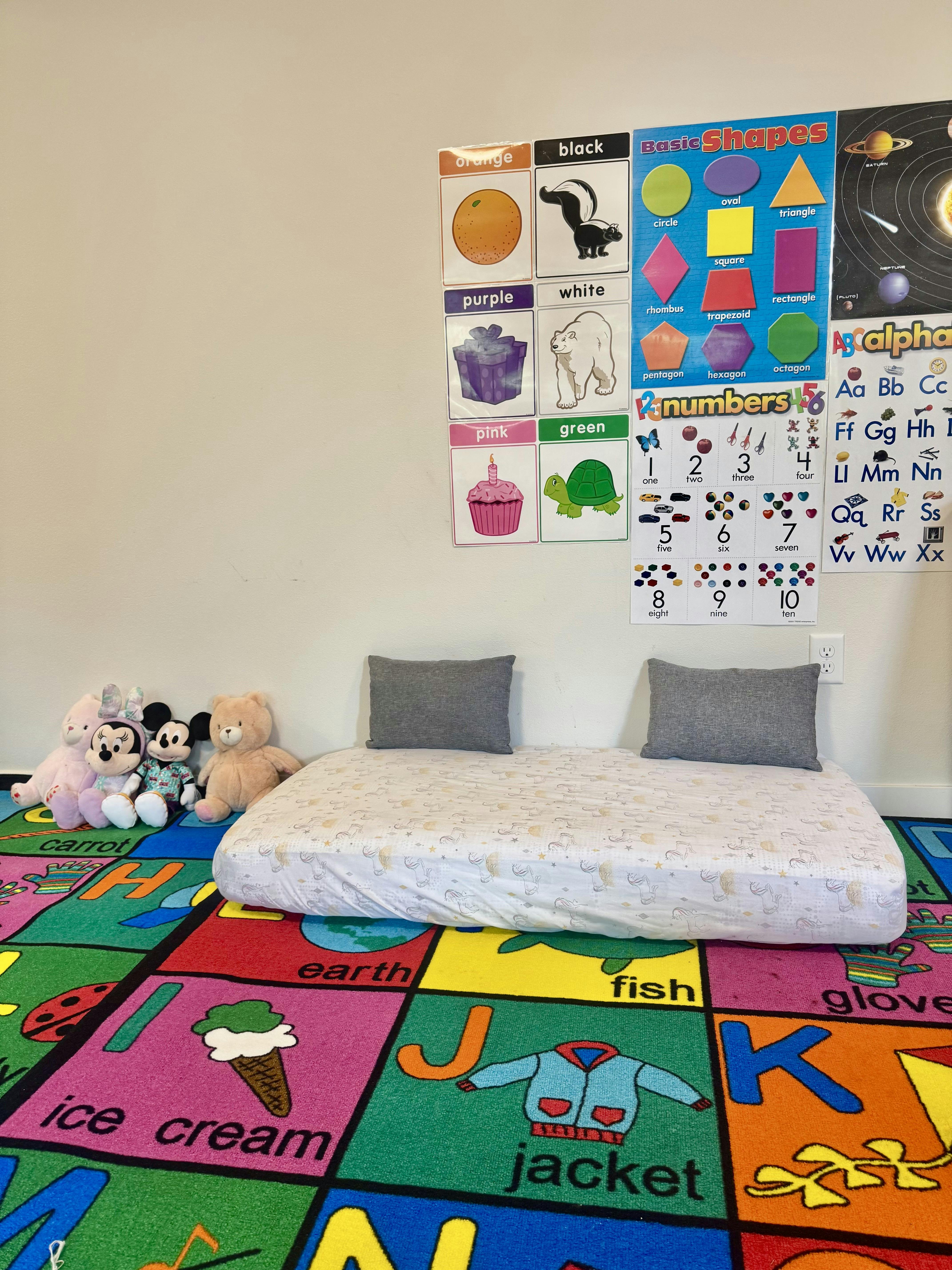 Low bed with pillows on a colorful alphabet rug in a playroom