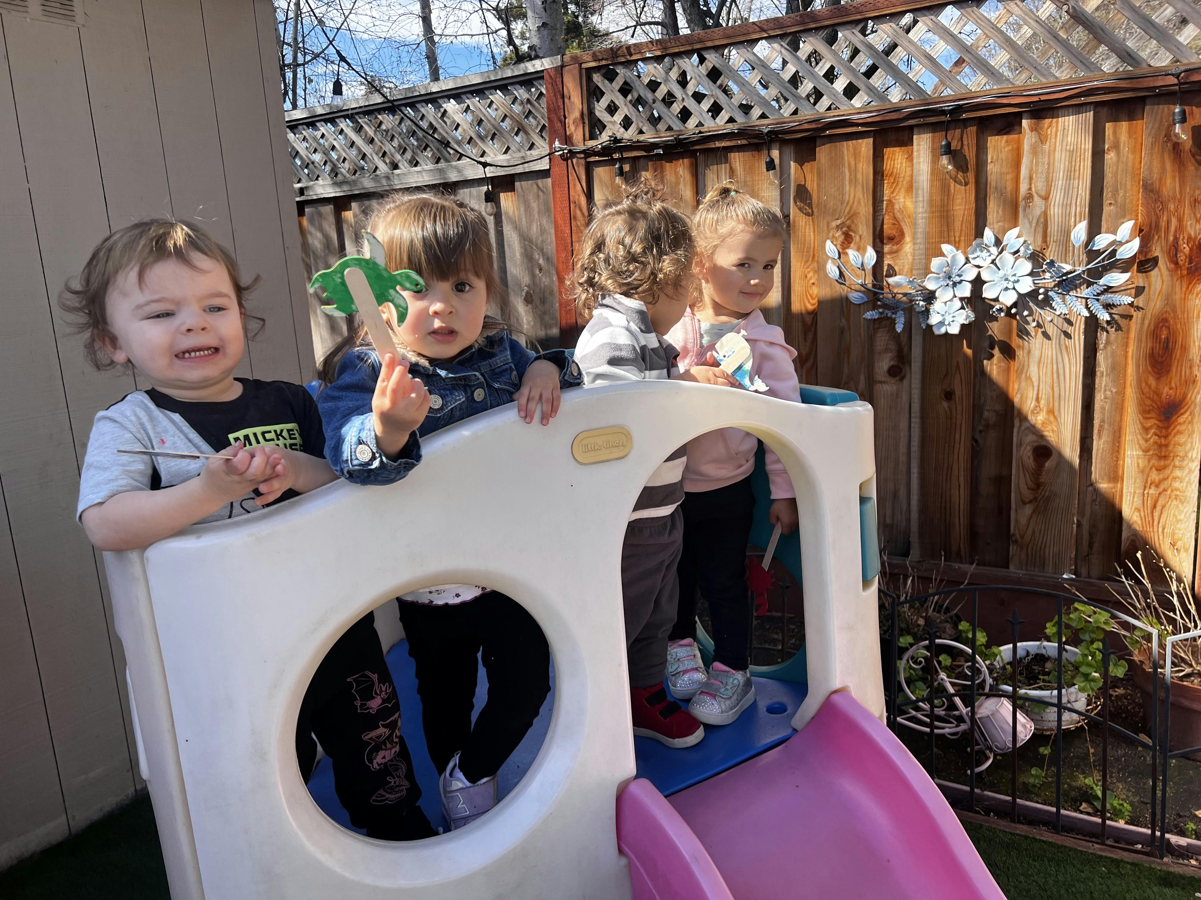 Four children in a small play structure with a pink slide