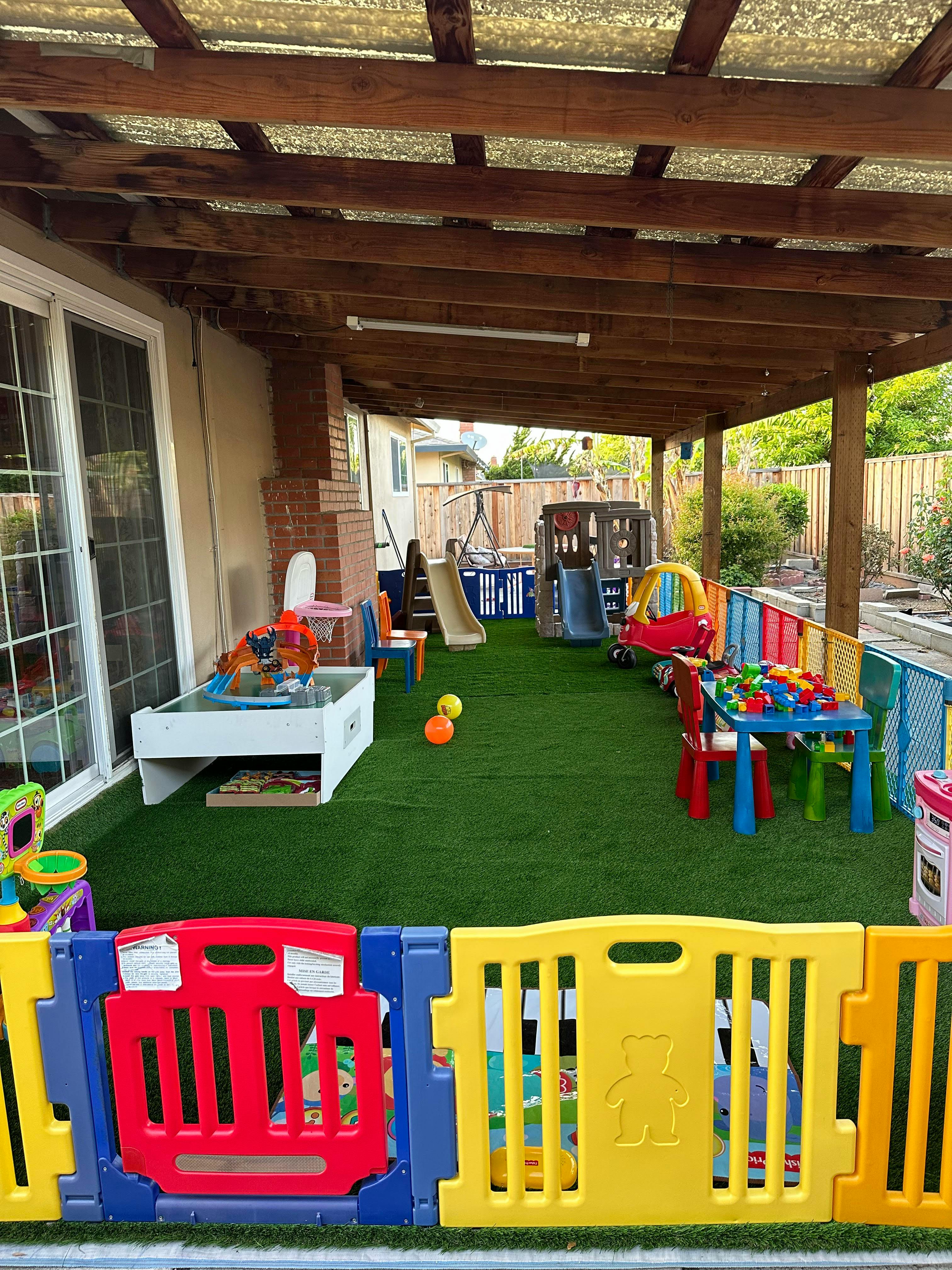 Play area with artificial turf, slides, a small table with blocks, and fencing