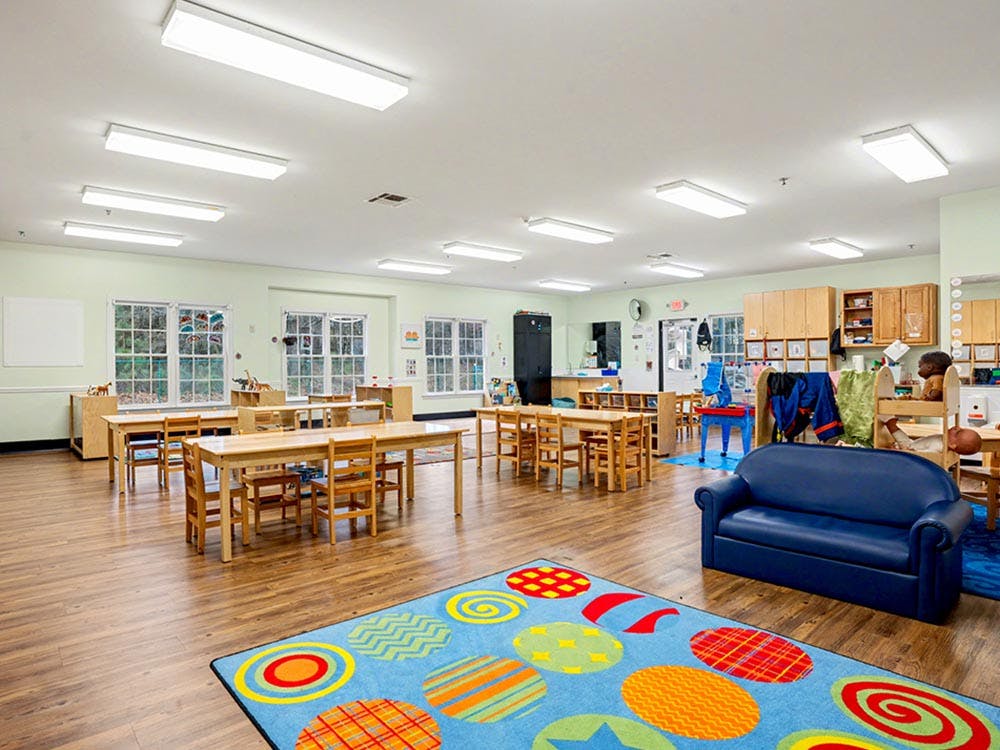 Classroom with small wooden tables and chairs, a blue couch, and a colorful rug