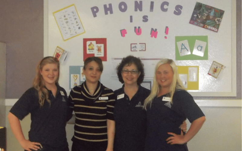 Four people standing in front of a whiteboard with "Phonics is Fun!" written on it