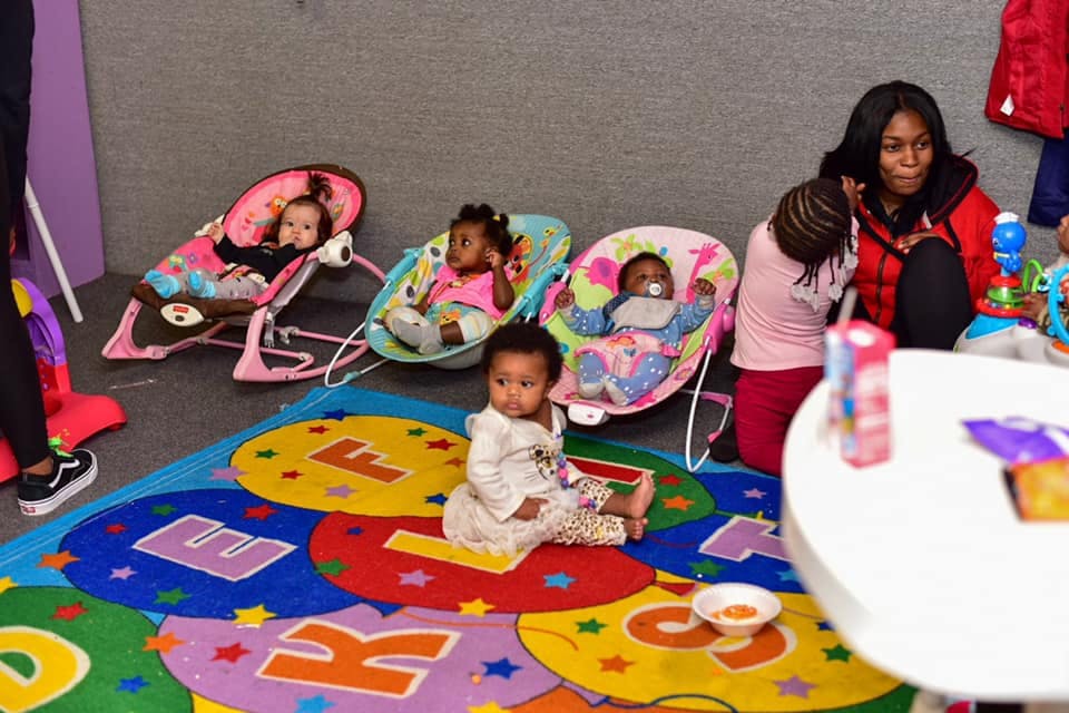 Adult and multiple babies in bouncers and on a colorful rug