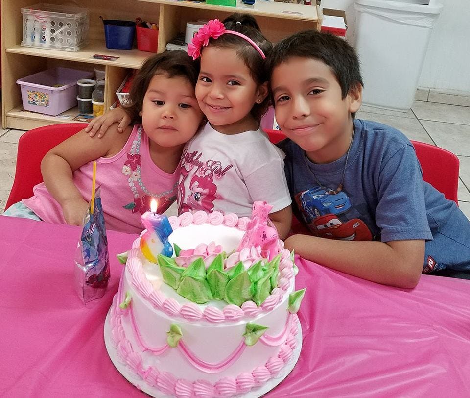 Three children sitting at a table with a birthday cake