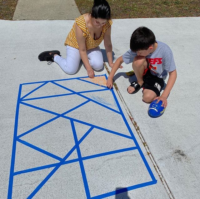 Person and child kneeling on pavement, placing tape to form a geometric pattern