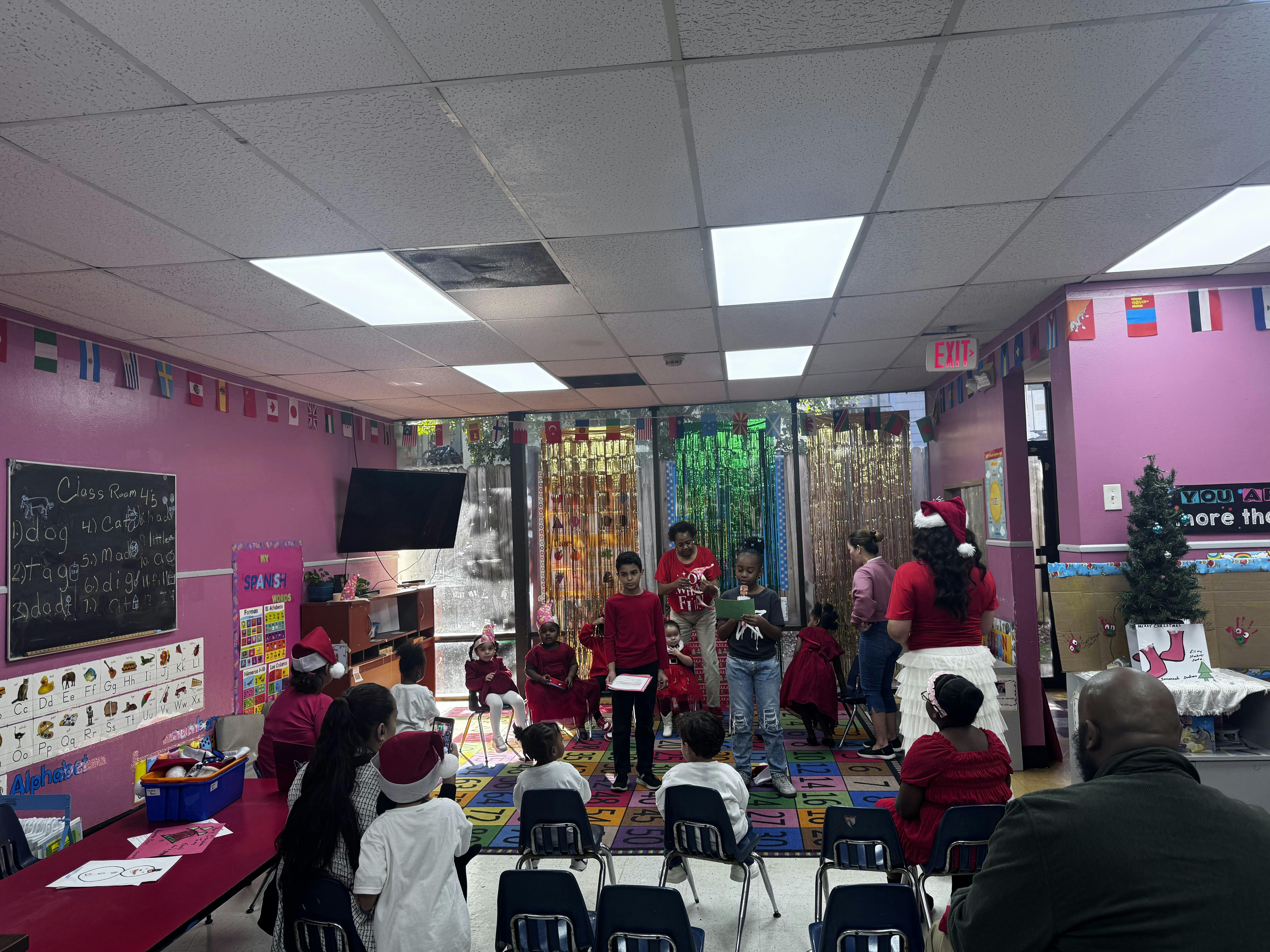 Children in a classroom, some wearing Santa hats, gathered for an event