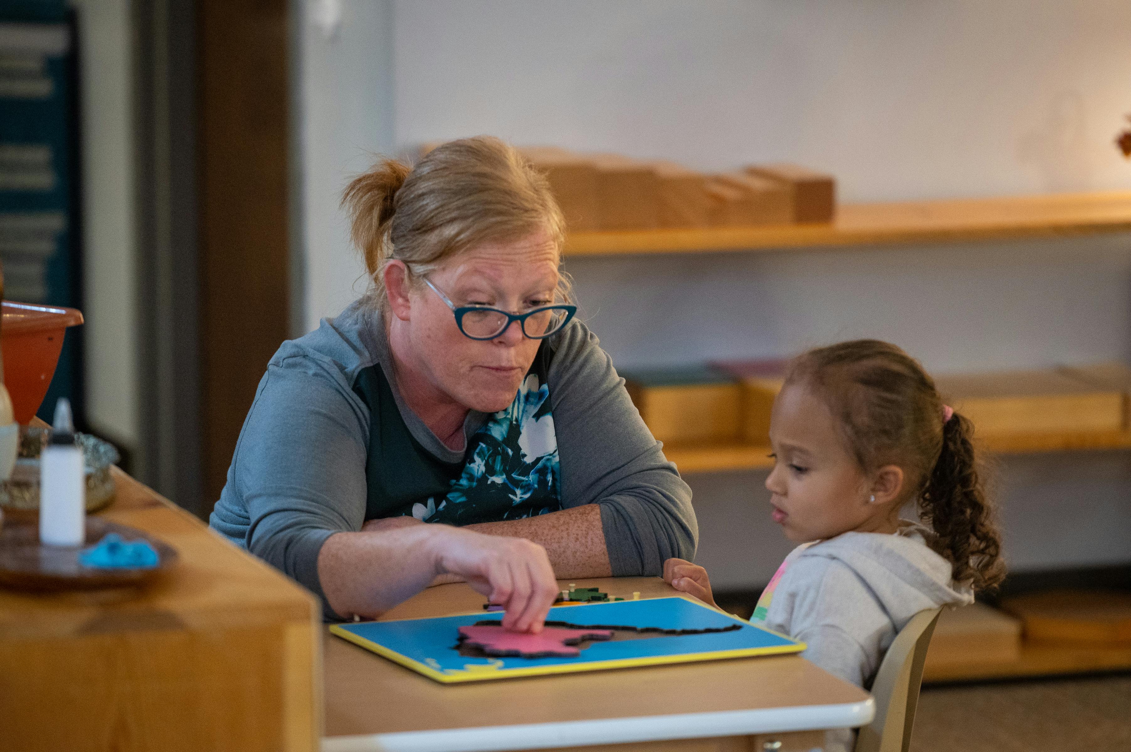 Person and child at a table, person pointing to a puzzle piece